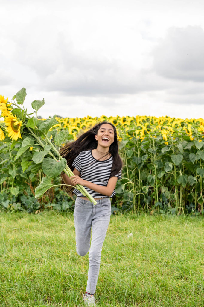 A girl laughing and running through a flower field holding sunflowers