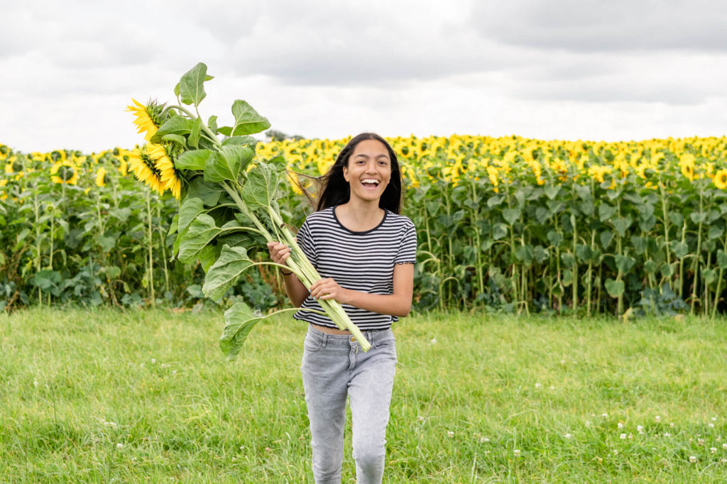 A girl running towards the camera holding sunflowers