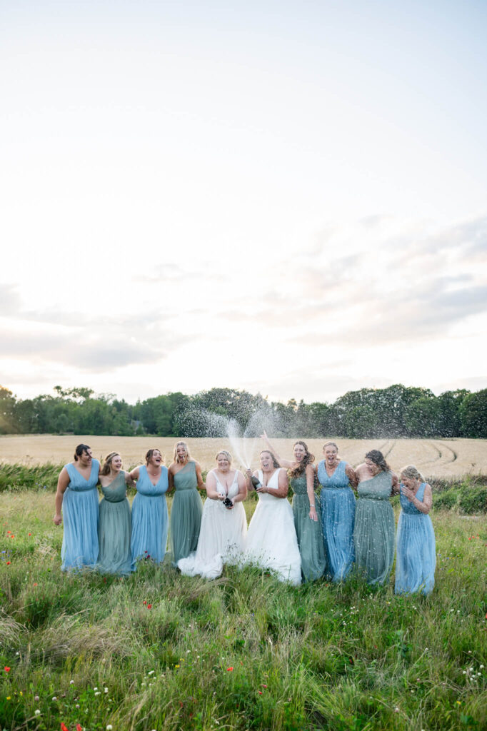 LGBTQ Wedding Photographer Chloe Bolam. Two brides and their bridesmaids doing a champagne spray
